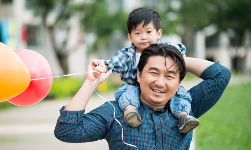 An Asian father hold his toddler son on his shoulders