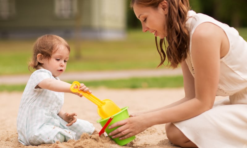 A mother and daughter play together in a sandbox