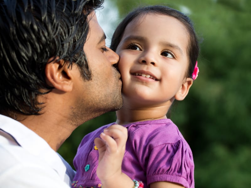 A south Asian father kisses his daughter's cheek