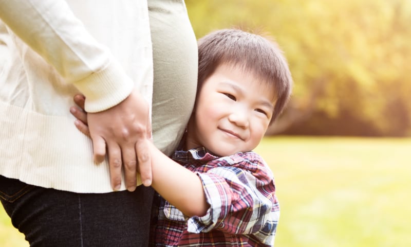 A young Asian boy hugs his pregnant mother