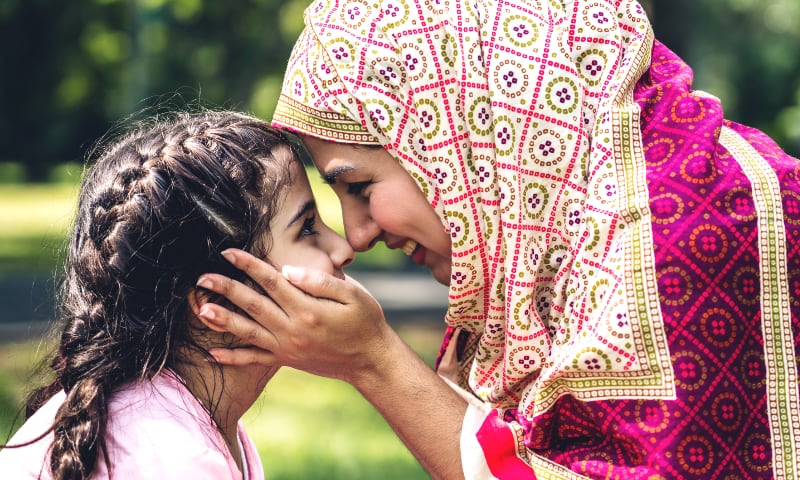 A Muslim mother with a head covering holds her smiling daughter