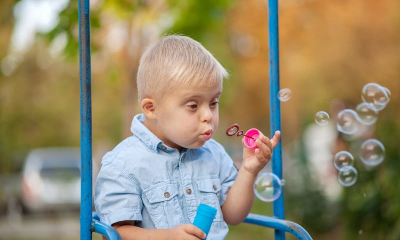 A small boy with Down syndrome sits on a swing and blows bubbles