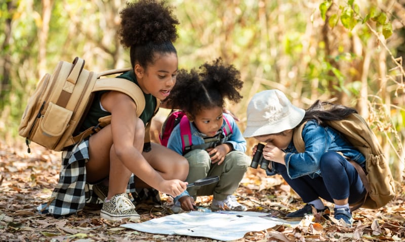 Three young children play in the woods, looking at a map